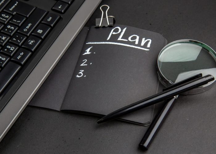 bottom-view-plan-written-black-notepad-lupa-keyboard-binder-clip-pen-black-background